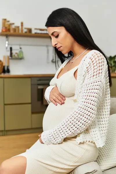 A beautiful young woman gently cradles her baby bump while enjoying a moment of peace in her home. — Stock Photo