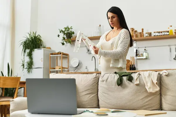 Expecting mother sorts through baby clothes while enjoying a cozy afternoon in her living room. — Stock Photo