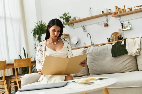 In a chic living room, a serene young woman reviews materials while embracing her pregnancy. — Stock Photo