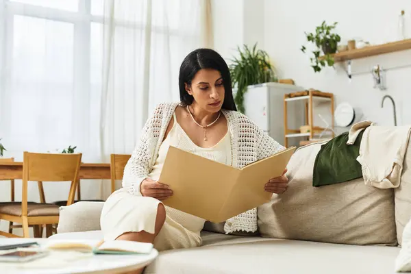 Young and beautiful pregnant woman sits on a sofa, looking at important papers in her home. — Stock Photo