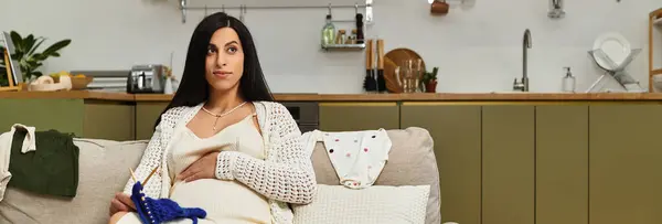 Pregnant woman sits on a sofa, knitting happily in her calm home. — Stock Photo