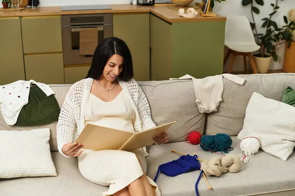 A young woman relaxes on a cozy couch, happily browsing crafting patterns during her pregnancy. — Stock Photo