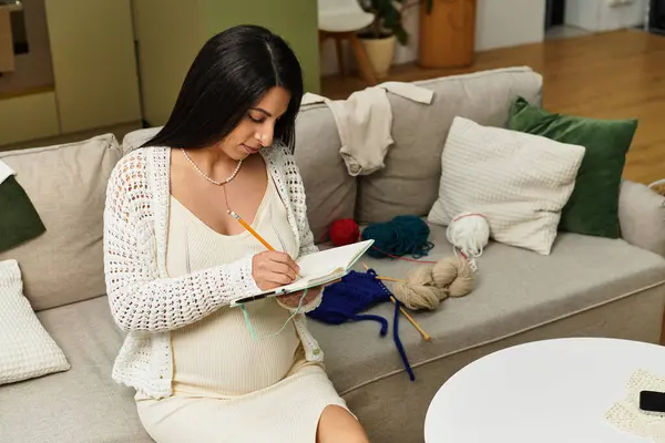 Junge schwangere Frau widmet sich kreativem Schreiben in einem ruhigen Raum voller Garn und Komfort. — Stockfoto