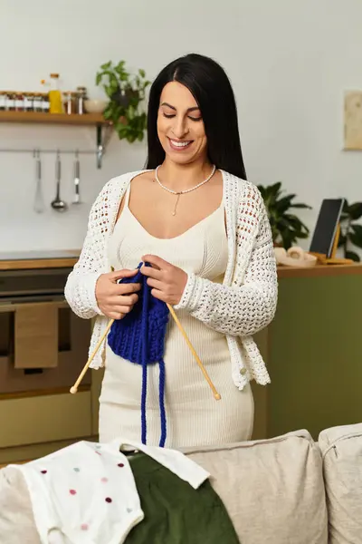 A beautiful young woman creates a knitted piece, smiling as she prepares for motherhood in her home. — Stock Photo