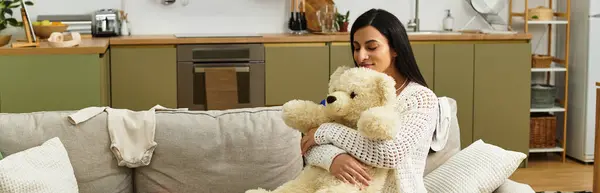 Expecting mother with long hair holds a fluffy teddy bear while sitting on a comfortable couch. — Stock Photo