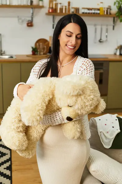 A young, beautiful pregnant woman smiles gently, holding a large teddy bear with joy. — Stock Photo