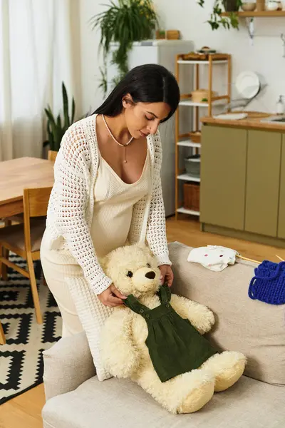Une jeune femme enceinte habille un ours en peluche dans un salon confortable pour son nouveau-né. — Photo de stock