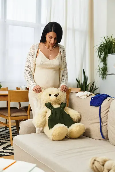 Jeune femme rayonnante interagit doucement avec un ours en peluche tout en se préparant à la maternité. — Photo de stock
