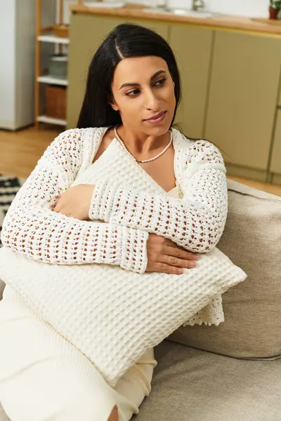 A young woman in a cozy knit top cradles a soft pillow, embracing a moment of tranquility at home. — Stock Photo