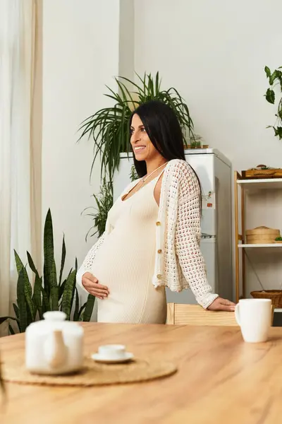 Young, beautiful woman in a cozy space gently cradles her baby bump, radiating joy. — Stock Photo