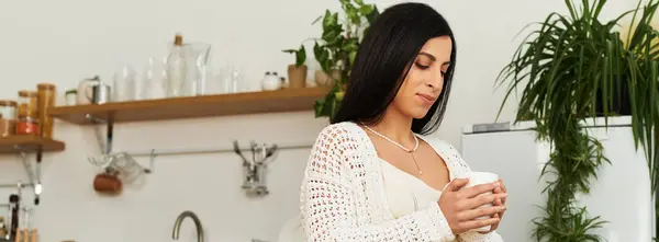 Eine schöne junge Frau in einer gemütlichen Küche hält eine warme Tasse und umarmt ihre Schwangerschaftsreise. — Stockfoto