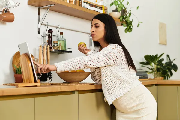 Uma jovem mulher em uma cozinha acolhedora prepara um lanche enquanto relaxa e desfruta de sua gravidez. — Fotografia de Stock