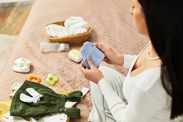 Esperar a la madre organiza cuidadosamente la ropa y los artículos del bebé en una habitación cálida y acogedora. - foto de stock