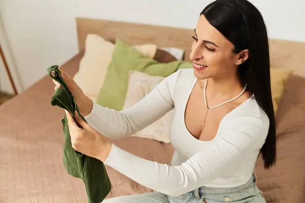 Expecting mother smiles warmly as she lovingly holds a piece of baby clothing in a serene setting. — Stock Photo