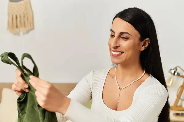 Giovane donna esamina gioiosamente i vestiti del bambino nel suo caldo, invitante spazio vitale, pieno di amore. — Foto stock