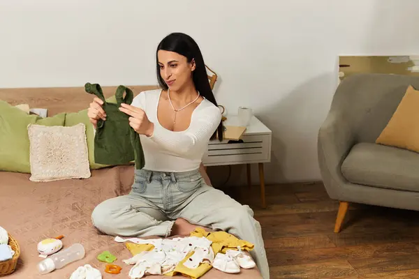 A pregnant woman sits on a bed, sorting through baby clothes in a peaceful moment. — Stock Photo