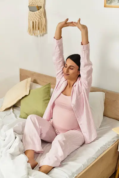 A young woman in pink loungewear stretches peacefully, embracing her pregnancy in her bedroom. — Stock Photo