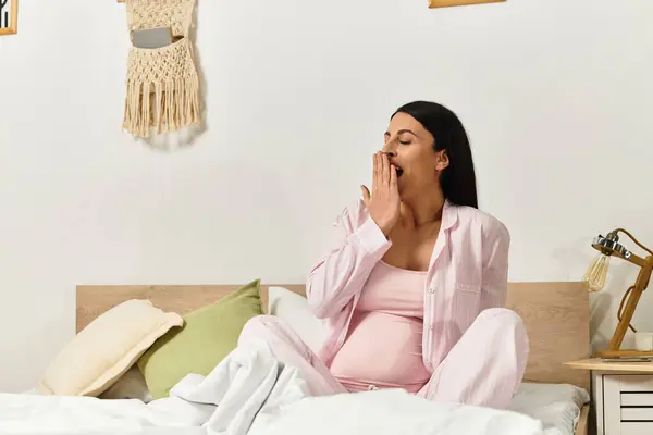 Jovem mulher de pijama rosa senta-se confortavelmente em seu quarto, abraçando a alegria da maternidade. — Fotografia de Stock