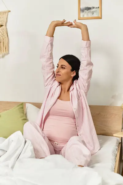 A radiant pregnant woman stretches joyfully in her serene bedroom as sunlight streams in. — Stock Photo