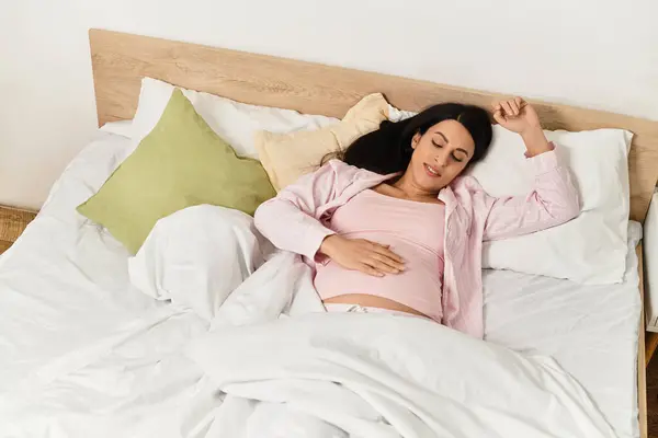 Relaxando na cama, a jovem mulher embala suavemente seu bebê colisão enquanto desfruta de tranquilidade. — Fotografia de Stock
