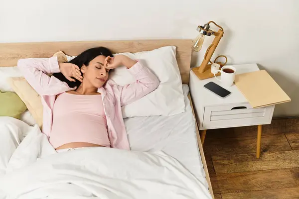 Eine junge Frau ruht friedlich im Bett und wiegt ihre Schwangerschaft sanft, während sie von Komfort umgeben ist. — Stockfoto