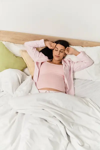 Young woman in pink top enjoys a tranquil moment while resting in bed, embracing her pregnancy. — Stock Photo