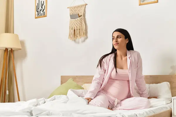 Woman in light pink attire sits on a bed, radiating serenity and anticipation in a bright room. — Stock Photo