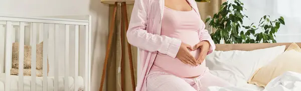 A young and beautiful woman in a cozy bedroom gently cradles her baby bump, radiating happiness. — Stock Photo