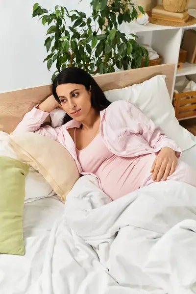 A beautiful young woman in a pink outfit rests on a bed, dreaming about motherhood. — Stock Photo