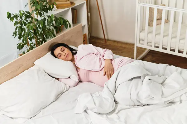 Uma jovem mulher em uma roupa rosa embala suavemente seu bebê colisão enquanto descansa na cama. — Fotografia de Stock