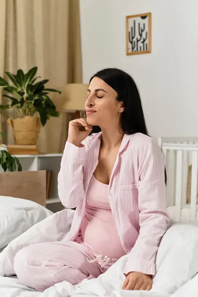 Beautiful pregnant woman sits on bed in a tranquil bedroom, savoring a serene moment. — Stock Photo