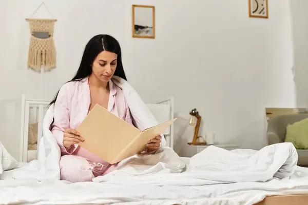Schöne schwangere Frau genießt ruhige Zeit in ihrem Zimmer, eingetaucht in ein fesselndes Buch auf ihrem Bett. — Stockfoto