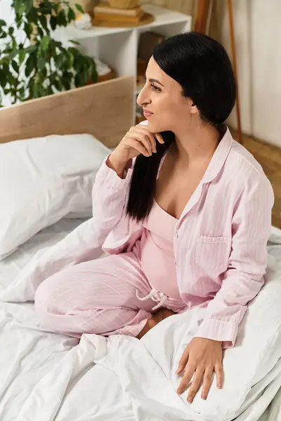 Mujer embarazada en pijama acogedor se refleja en un entorno sereno, rodeado de ropa de cama suave y vegetación. - foto de stock