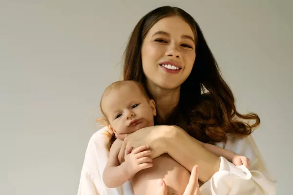 Una bella giovane madre stringe il suo bambino sorridente, irradiando amore e felicità in un'atmosfera calma. — Foto stock