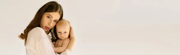 Una giovane madre guarda teneramente lo spettatore mentre culla il suo bambino, irradiando calore.. — Foto stock