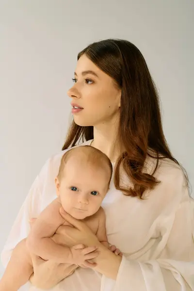A young mother cradles her adorable child, radiating love and warmth in a serene environment. — Stock Photo