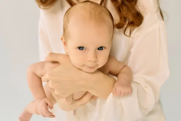 A serene young mother lovingly holds her cherubic child, radiating warmth and joy in their bond. — Stock Photo