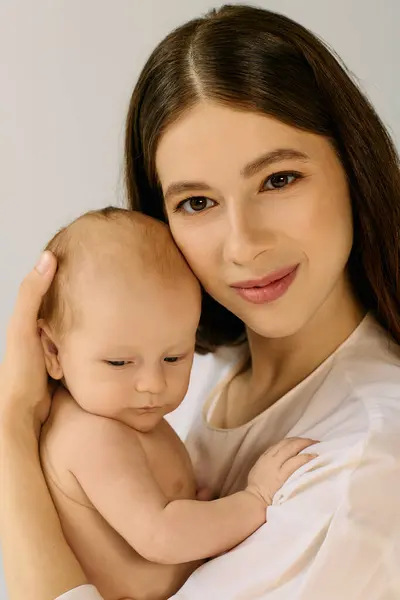 Una giovane madre tiene amorevolmente stretto il suo bambino, mostrando il loro legame in un ambiente calmo. — Foto stock