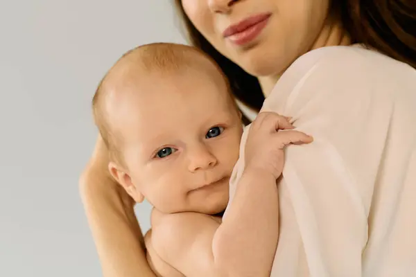 A loving young mother holds her child against a soft backdrop, radiating warmth and joy. — Stock Photo