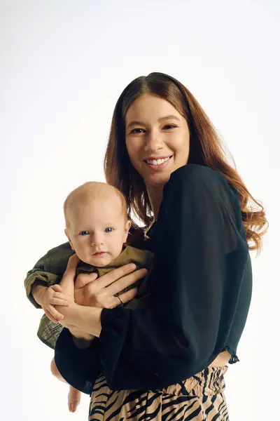 Una giovane madre tiene amorevolmente il suo bambino in uno studio luminoso, irradiando calore e felicità. — Foto stock