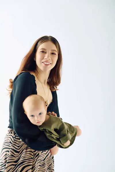 A beautiful young mother holds her little child in an embrace filled with joy and warmth indoor. — Stock Photo