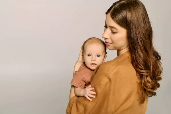 A young mother gazes lovingly at her baby while holding them close, radiating love and tenderness. — Stock Photo