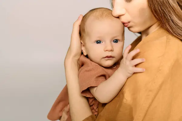 A young mother gently kisses her babys forehead while holding him close in a warm atmosphere. — Stock Photo