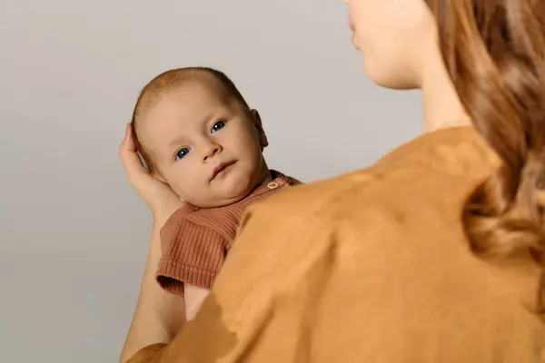 Una giovane madre tiene amorevolmente il suo bambino in un ambiente caldo e sereno. — Foto stock