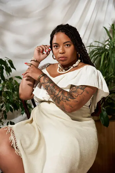Uma bela mulher afro-americana com tranças posa graciosamente em um vestido de verão entre plantas exuberantes. — Fotografia de Stock