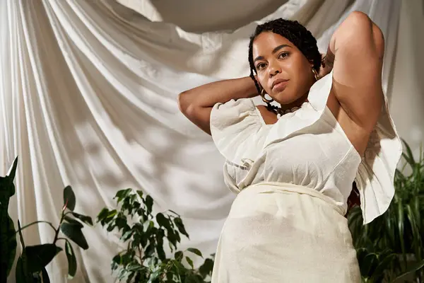 A stunning African American woman poses in a summer dress, surrounded by lush plants. — Stock Photo