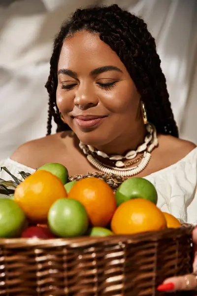 A joyful moment unfolds as a woman embraces a basket of colorful fruits amidst lush plants. — Stock Photo