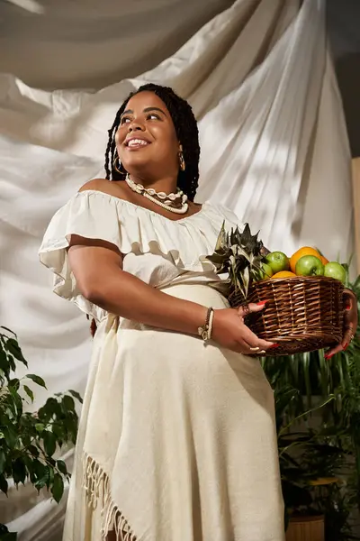 A radiant Black woman smiles, holding a basket of fresh fruit amidst lush greenery. — Stock Photo