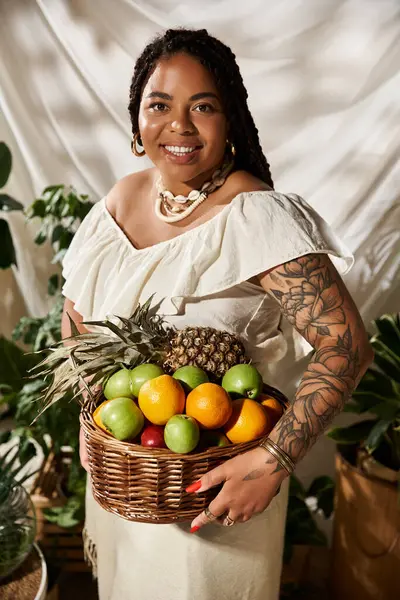 A stylish African American woman with braids presents a colorful fruit basket amid lush greenery. — Stock Photo