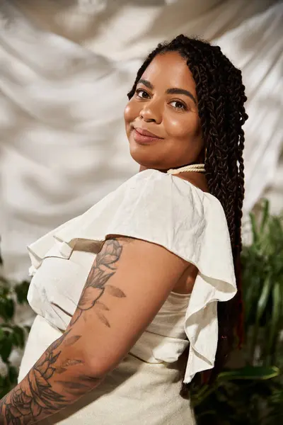 A pretty African American woman with braids poses gracefully amidst vibrant green plants. — Stock Photo